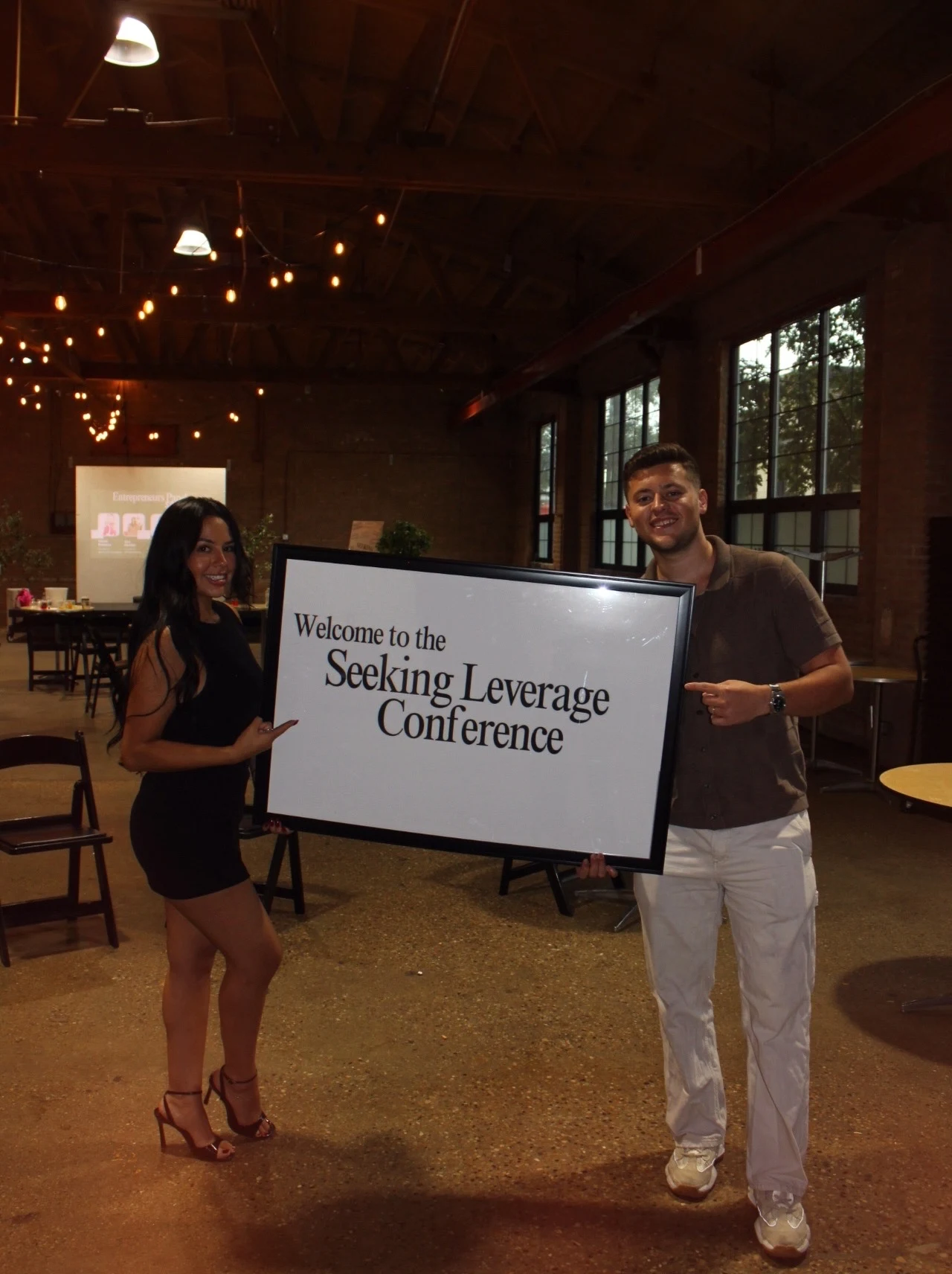 Michelle and a guest holding the Seeking Leverage conference welcome sign